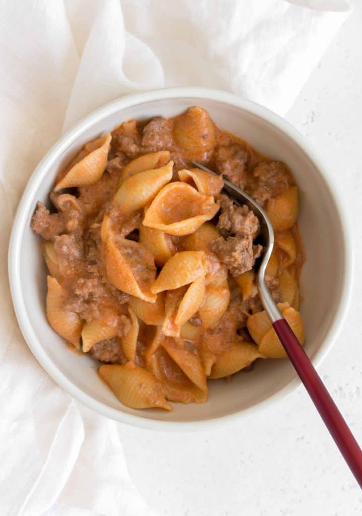 white bowl with creamy pasta shells with beef and a fork in the bowl.