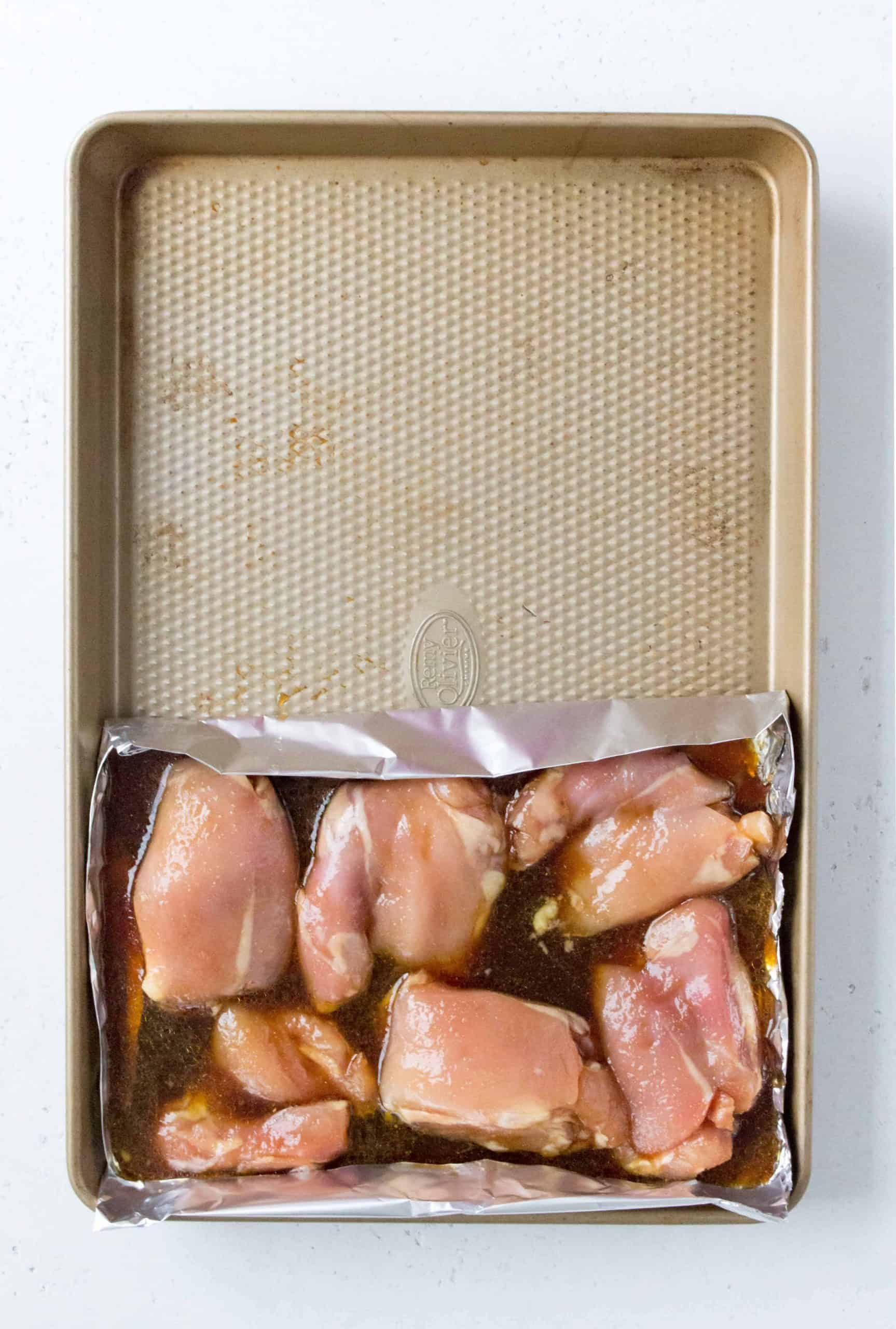 Overhead view of a sheet pan with chicken thighs with sauce. 