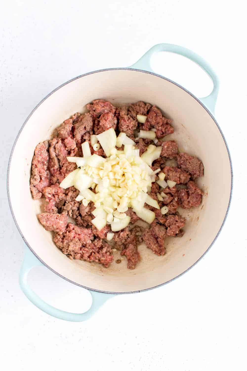 Diced onions and garlic added to ground beef in a pot.