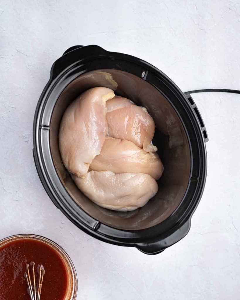 Chicken breasts added to a slow cooker.