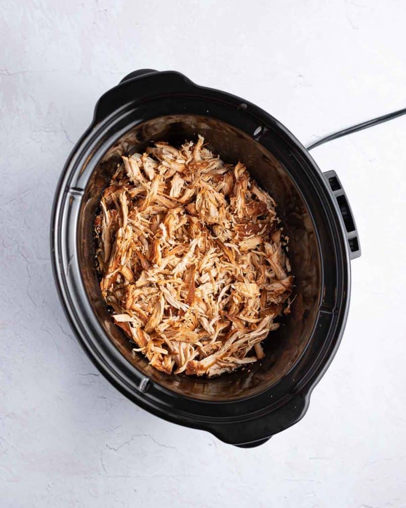 Overhead view of shredded chicken added back into the slow cooker.