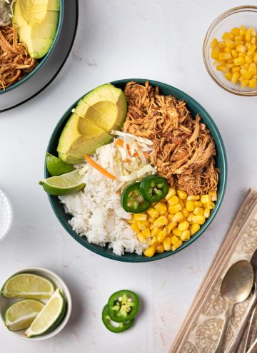 Overhead view of a bowl of shredded honey chipotle chicken with corn, avocado, and lime.