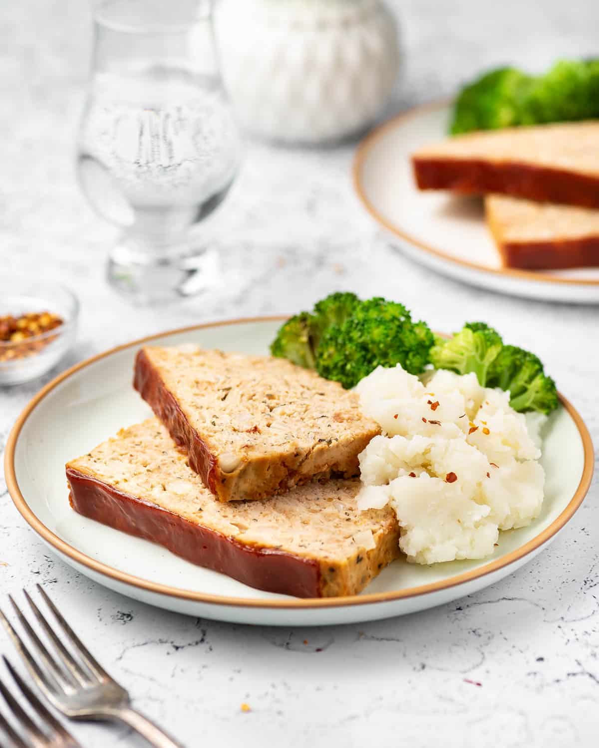 A plate with two slices of chicken meatloaf with mashed potatoes and broccoli.