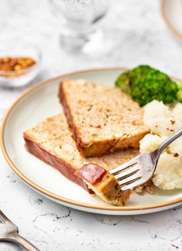 A plate with two slices of chicken meatloaf with mashed potatoes and broccoli with a fork lifting a bite.