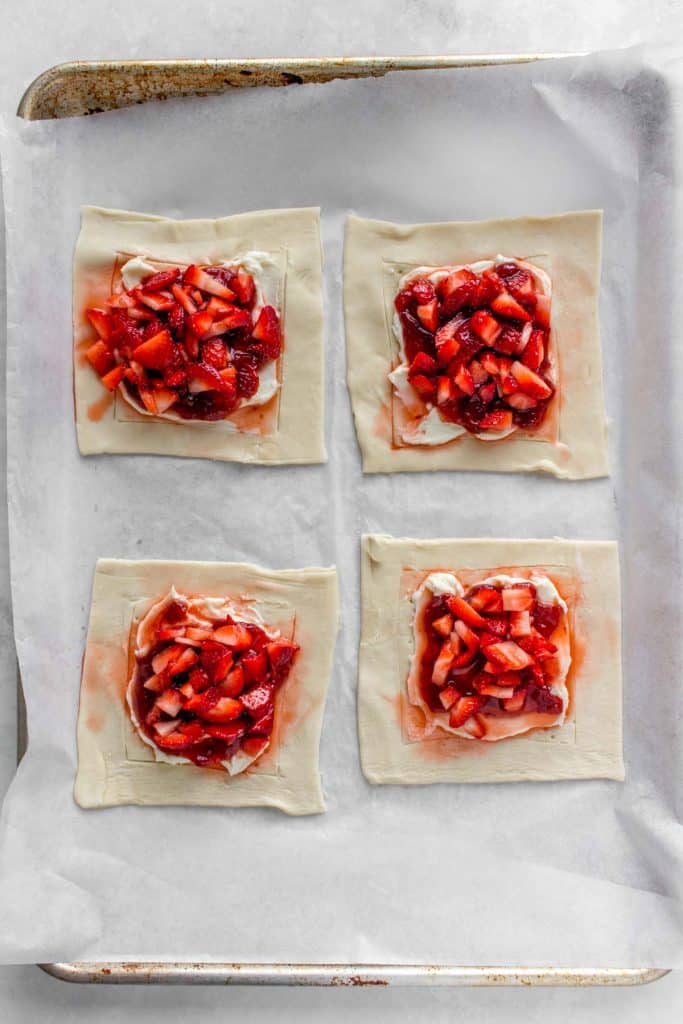 A sheet pan with four strawberry cheese danishes, before baking.
