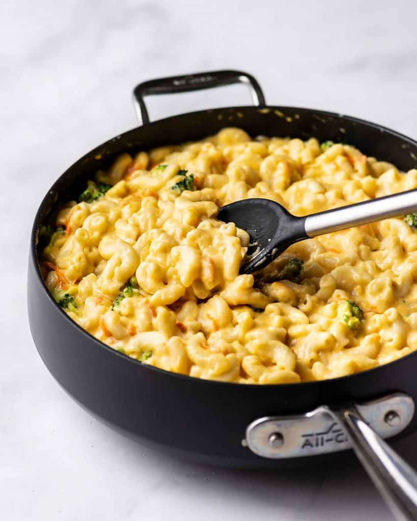 A spoon going into a pan of copycat panera broccoli cheddar mac and cheese.