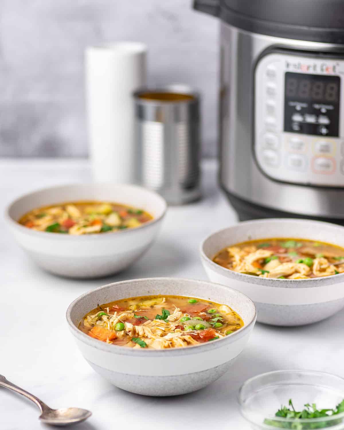 Three bowls of instant pot chicken vegetable soup in front of an instant pot.