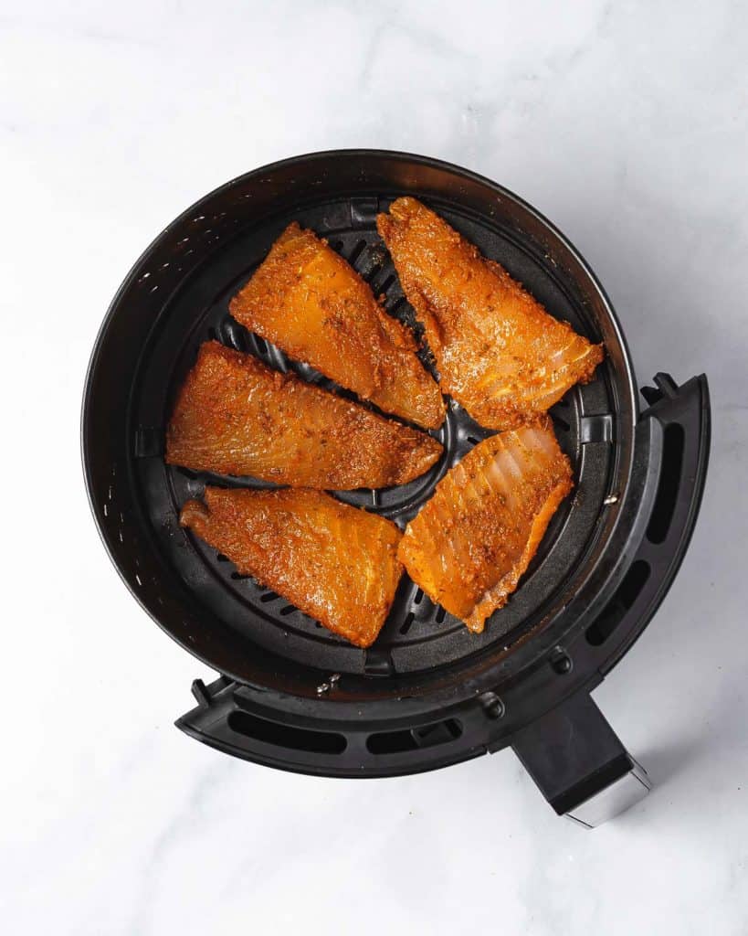 Air fryer basket with seasoned fish fillets.