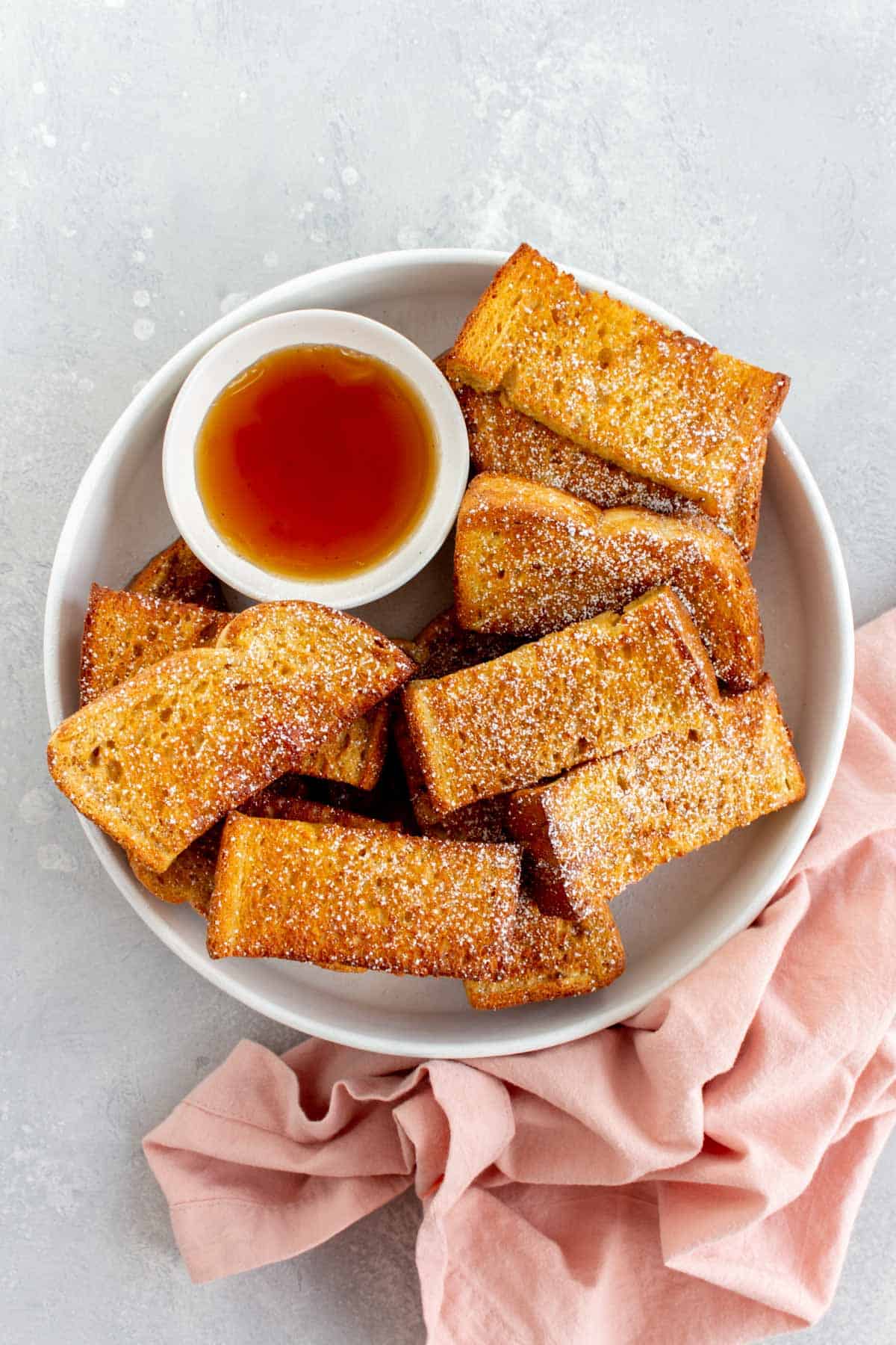 A plate of air fryer french toast sticks with powdered sugar dusted on top.