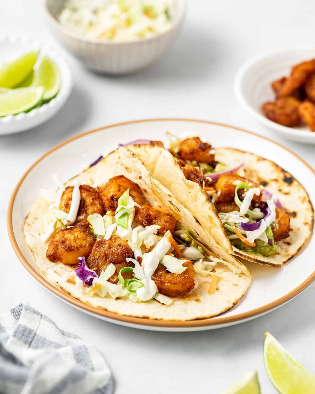 Close up view of two shrimp tacos on a plate topped with a drizzle of sauce. 