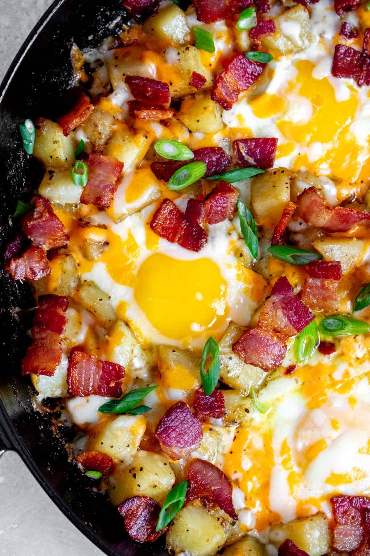 Close up of a skillet of diced potatoes, eggs, and bacon.