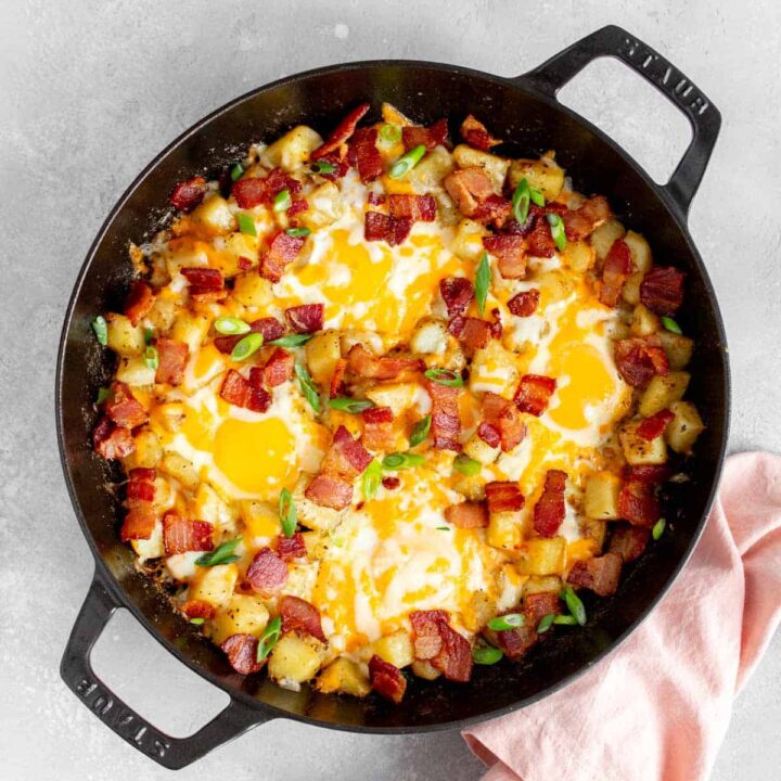 Overhead view of a skillet with diced potatoes, eggs, bacon, and green onions.