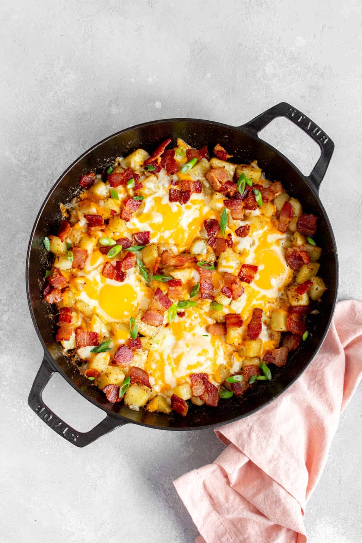 Overhead view of a skillet with diced potatoes, eggs, bacon, and green onions.