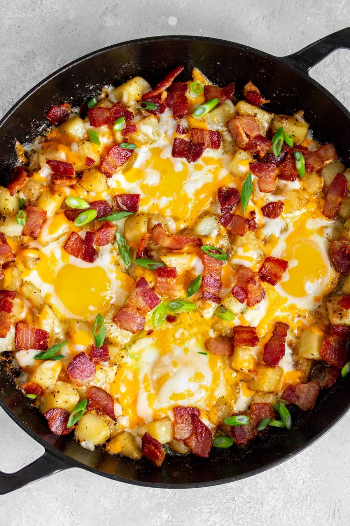 Close up of a skillet with bacon, eggs, and potatoes.