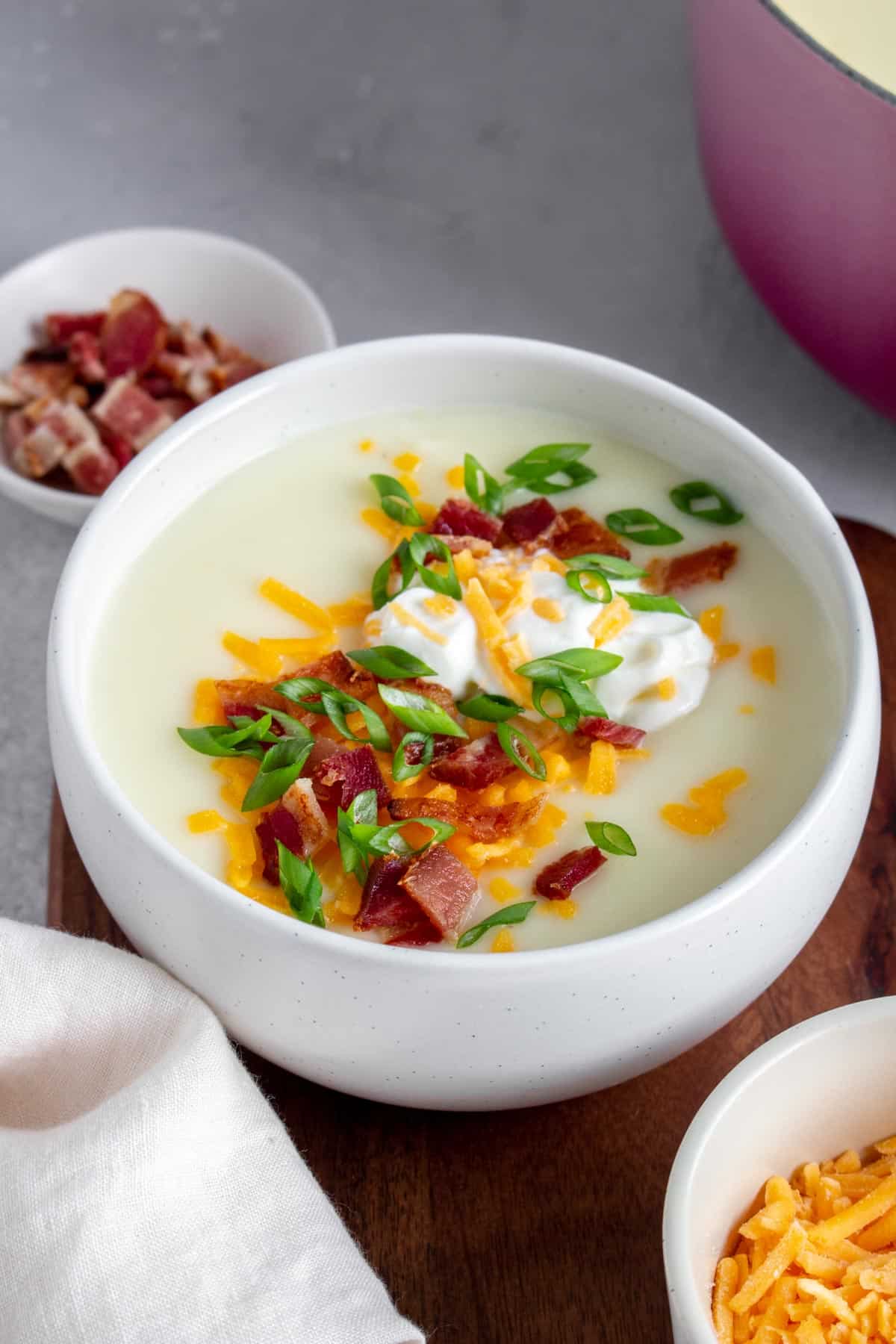 A bowl of potato soup with sour cream, shredded cheese, bacon, and green onions.
