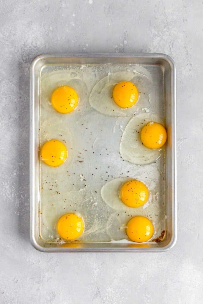 Eggs added to a sheet pan and seasoned with salt and pepper.