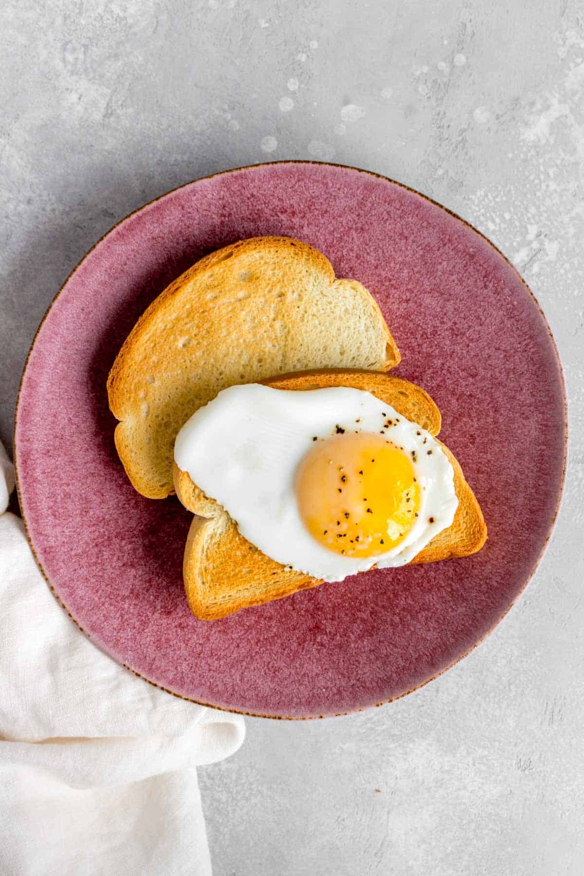 Two pieces of toast, one with an egg on top.
