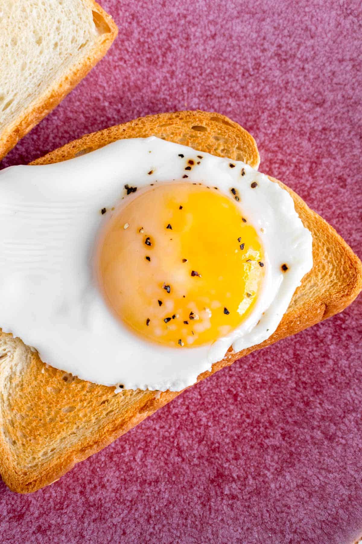 Close up of a sunny side up egg on a piece of toast.