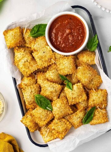 A tray of air fryer ravioli with a small bowl of dipping sauce on the side.