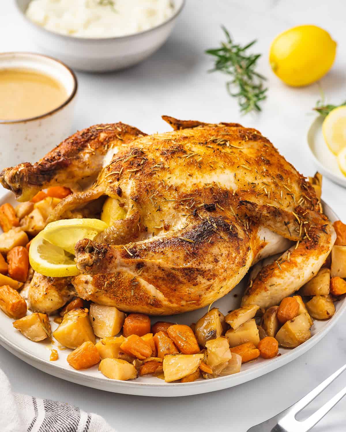 A slow cooker whole chicken surrounded by root vegetables on a large serving plate.