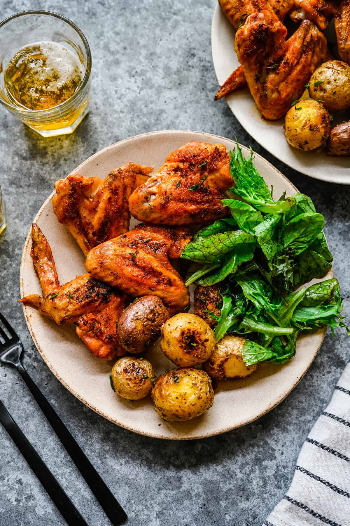 A plate with greens, potatoes, and baked whole chicken wings.