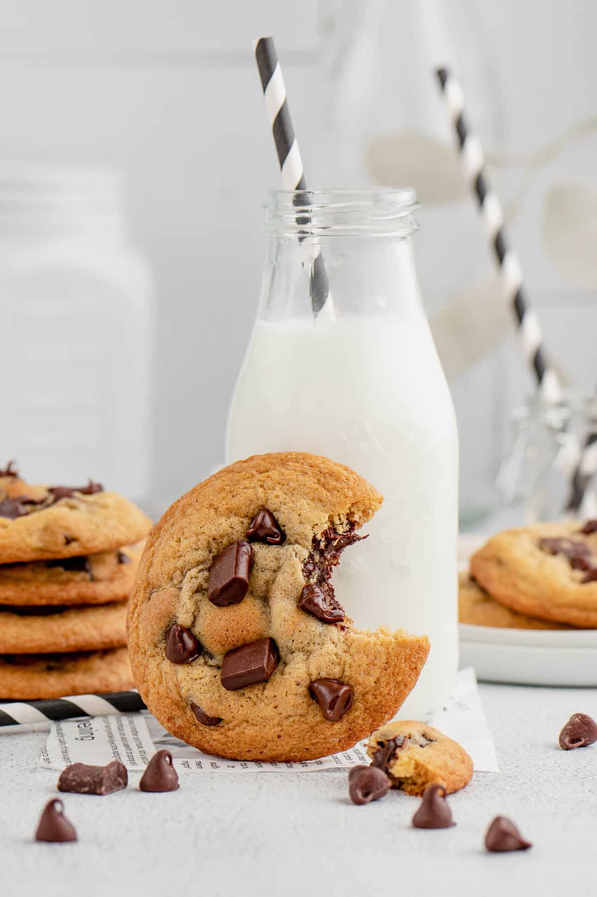 A chocolate chip cookie with a bite taken out leaned up against a glass of milk.