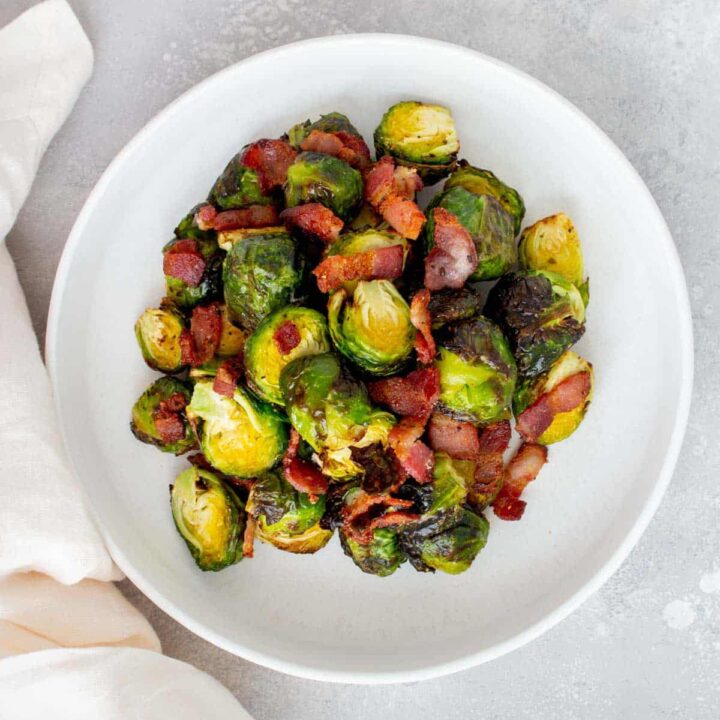 Overhead view of a white plate with air fryer brussels sprouts and bacon with a linen on the side.