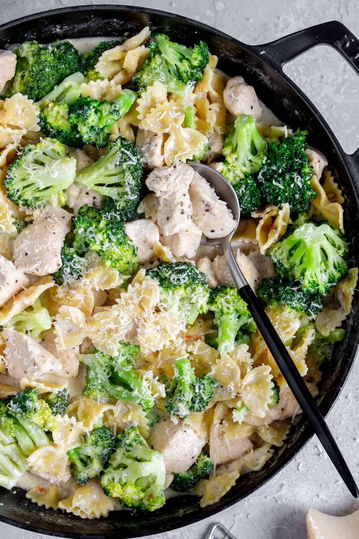 Overhead view of a large round pan of chicken broccoli alfredo with a spoon tucked in.