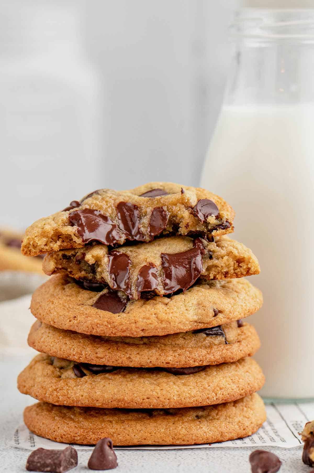 A slack of chocolate chip cookies with the top one torn in half and stacked.