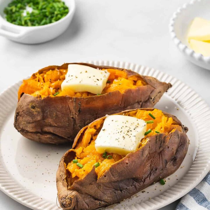 A plate with two slow cooker sweet potatoes with butter and chives on top.