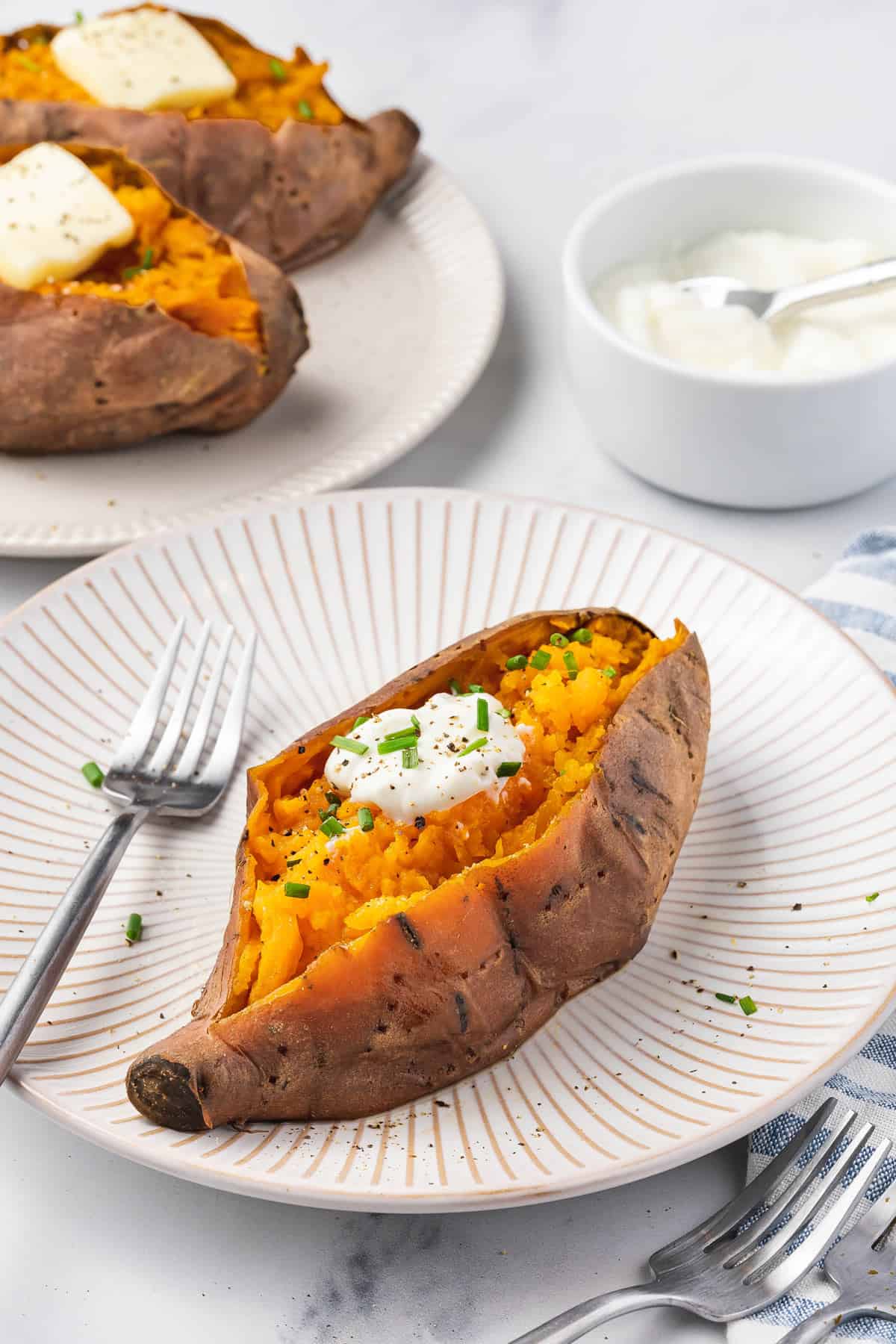 A plate with a slow cooker sweet potato with butter and chives on top.