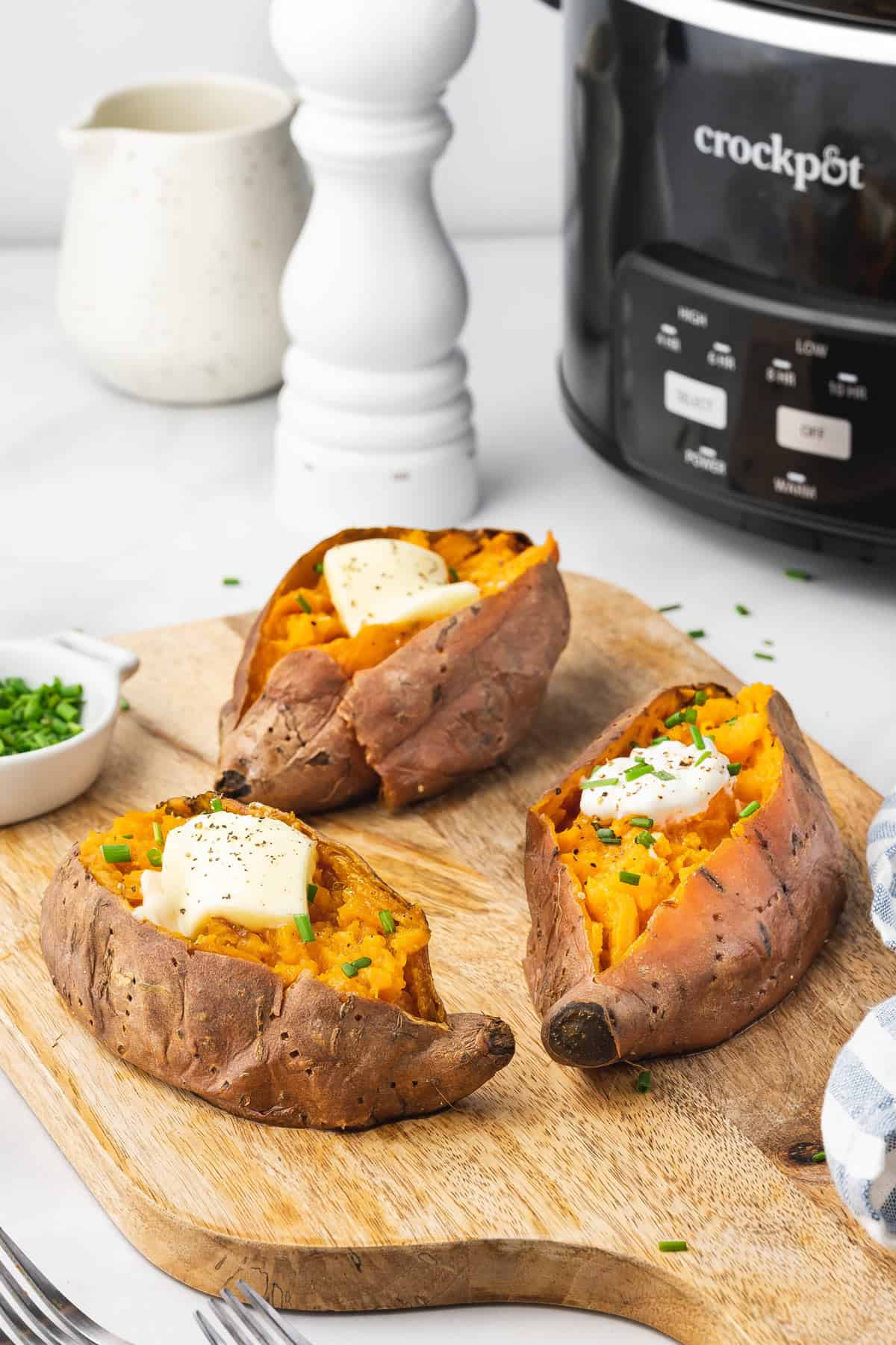Three slow cooker sweet potatoes with butter and chives on top.