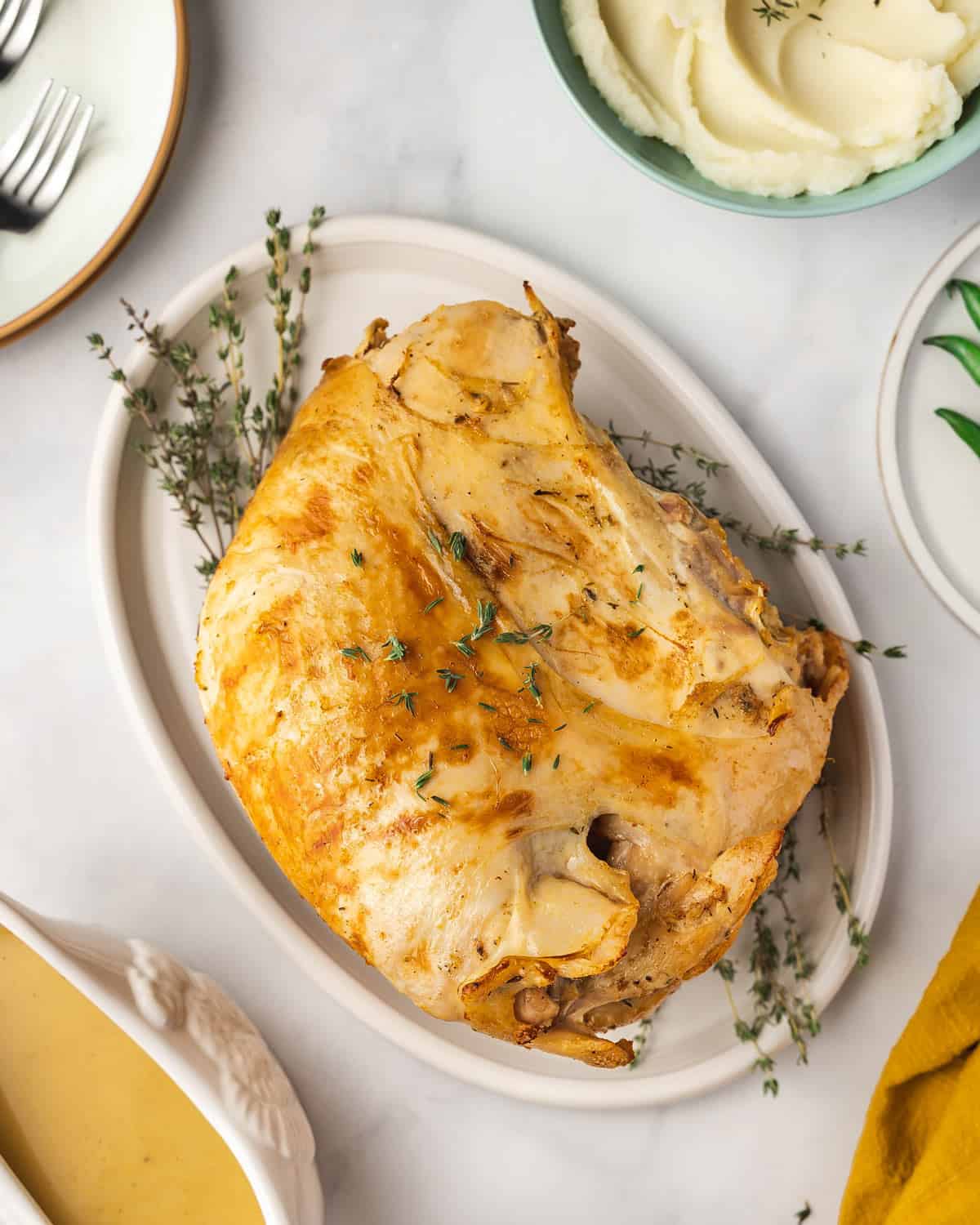 Overhead view of a slow cooker turkey breast on a white platter with fresh thyme underneath.