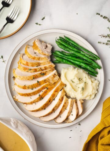 A large place with sliced slow cooker turkey breast with a side of mashed potatoes and green beans.