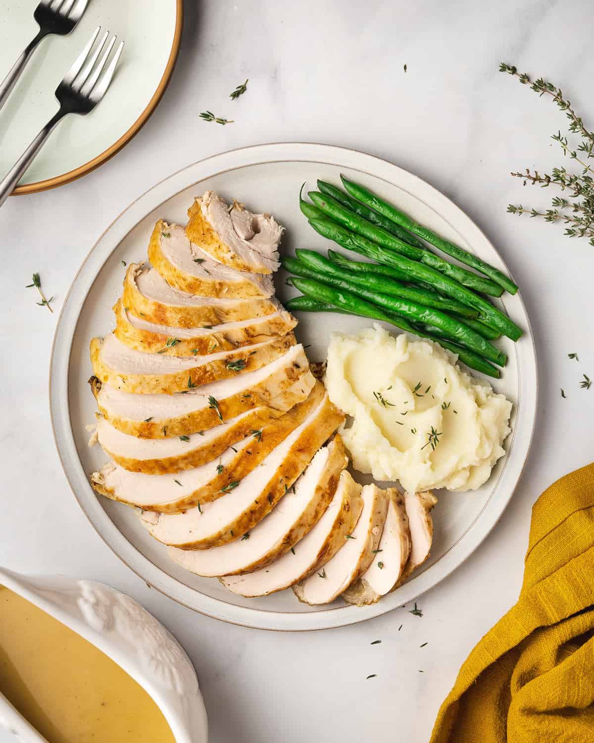 A large place with sliced slow cooker turkey breast with a side of mashed potatoes and green beans.
