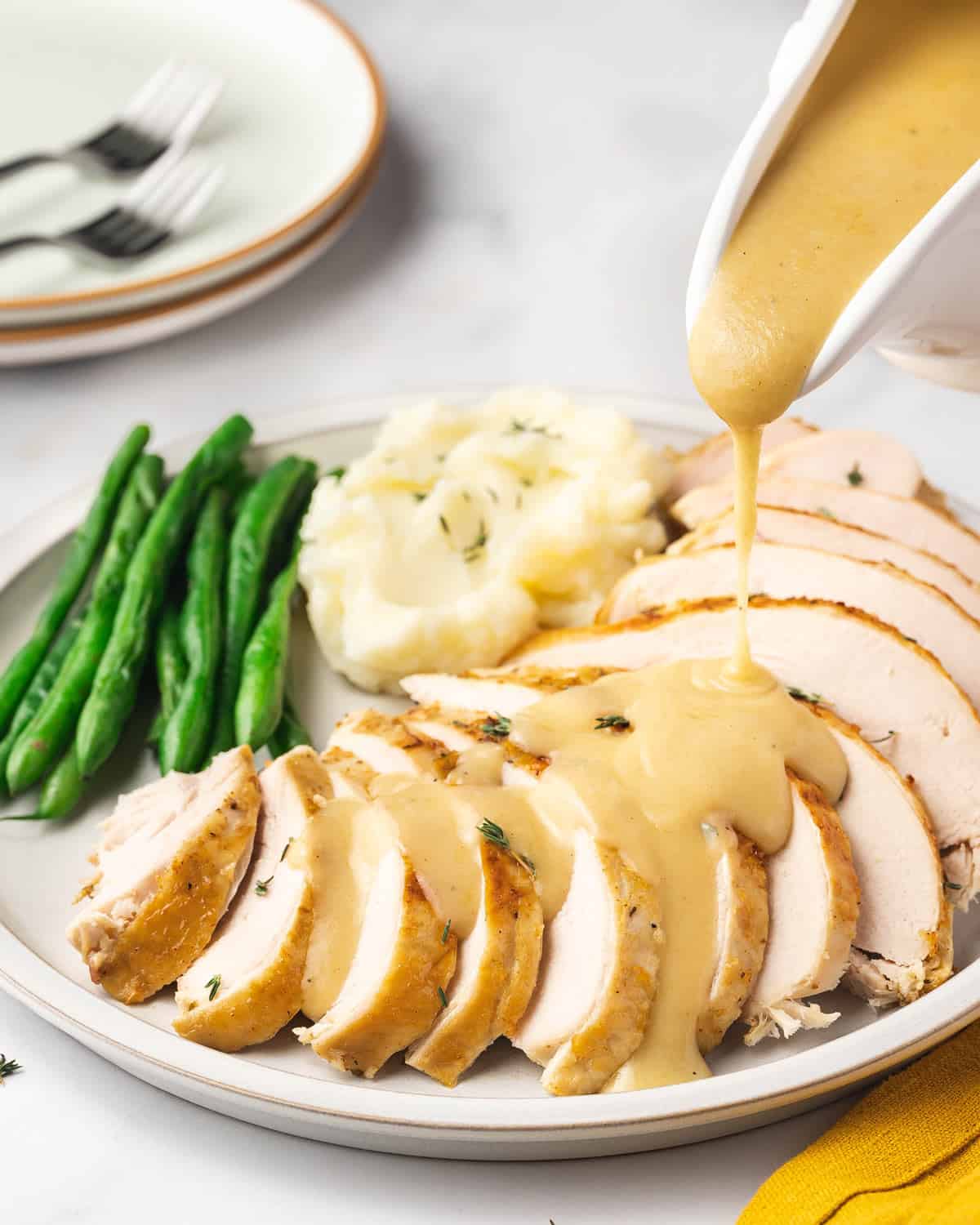 Gravy poured over a plate of sliced turkey breast cooked in a slow cooker with mashed potatoes and green beans on the same plate.
