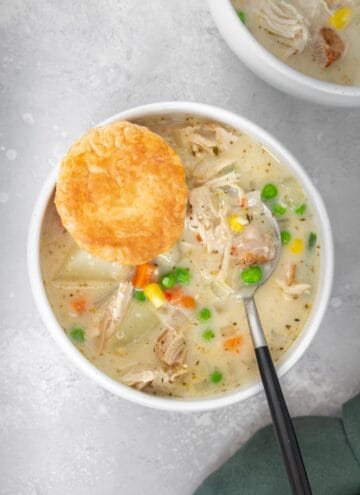 A bowl of turkey pot pie soup with a spoon and puff pastry inside.