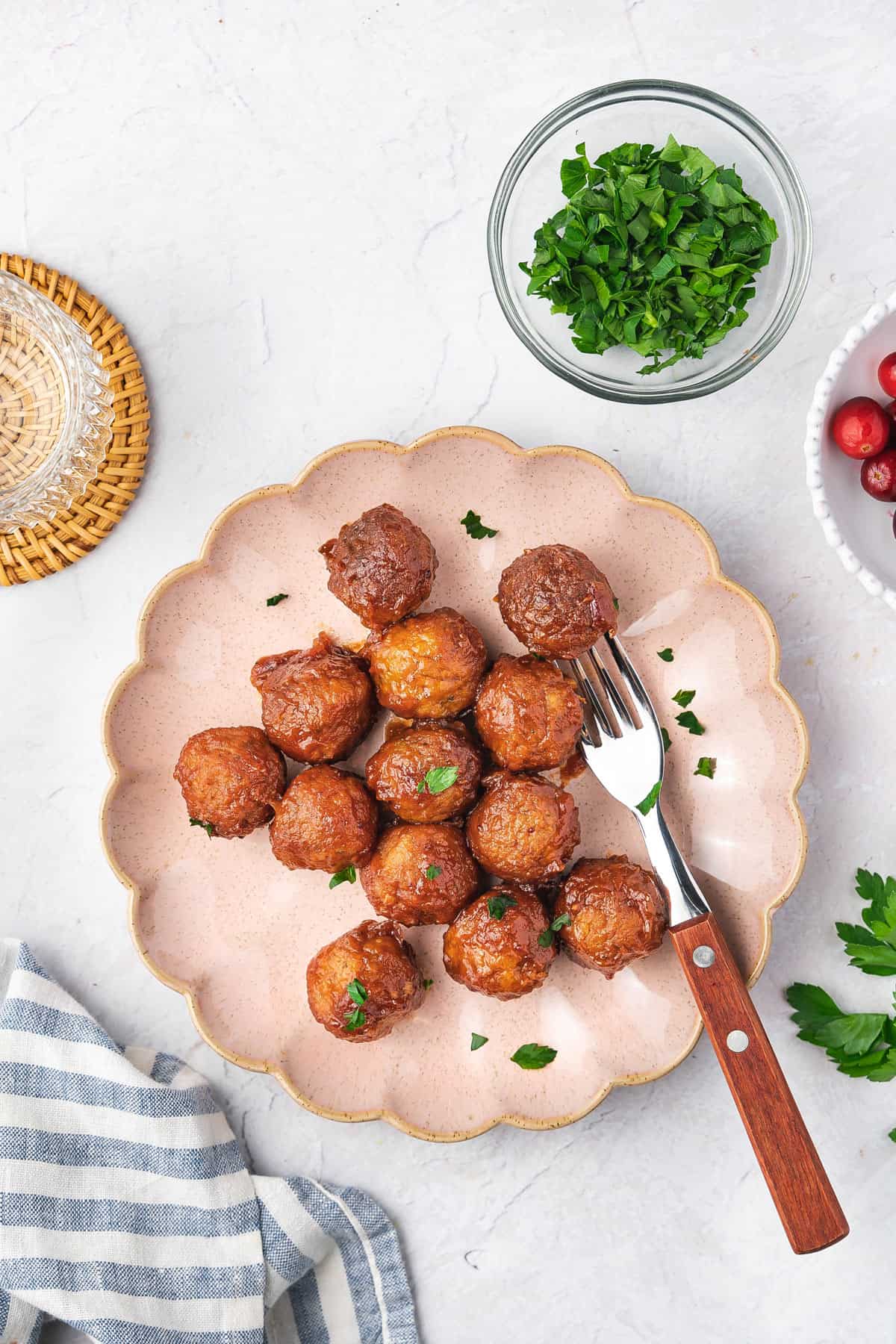 Overhead view of a scalloped plate with slow cooker cranberry meatballs and a fork.