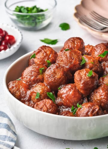 A bowl of slow cooker cranberry meatballs on top with fresh parsley garnish.
