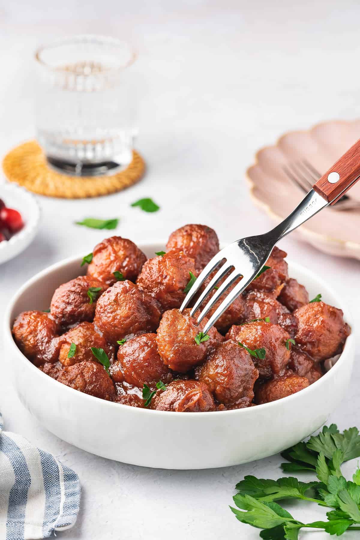A fork piercing into a cranberry meatball in a bowl.