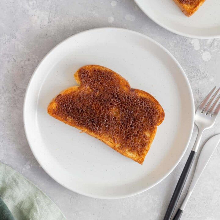 A plate with a piece of air fried cinnamon toast with a fork and knife beside it.