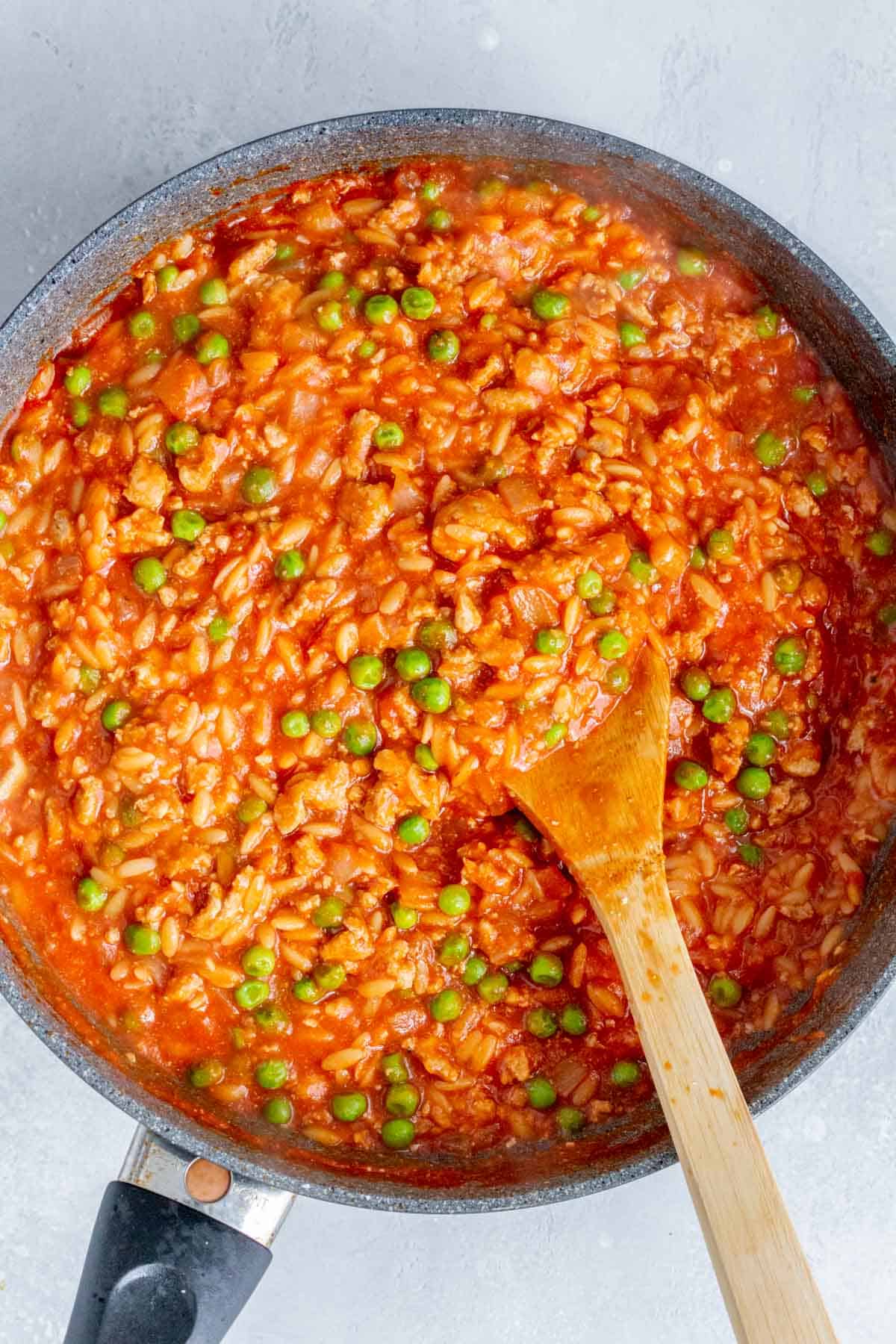 Overhead view of one pot orzo with turkey and peas being stirred in the skillet.