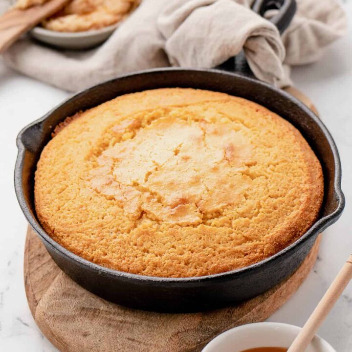 A skillet cornbread in a cast-iron skillet with a linen wrapped around the handle.