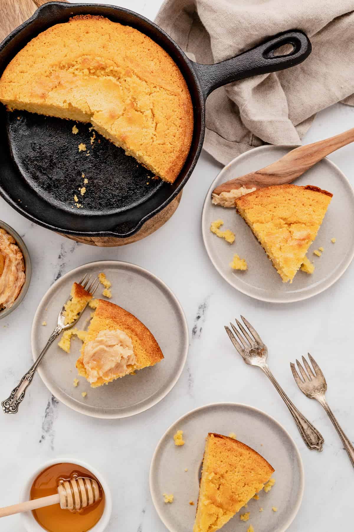 A skillet cornbread off to the side with three small plates, each with a slice on it.