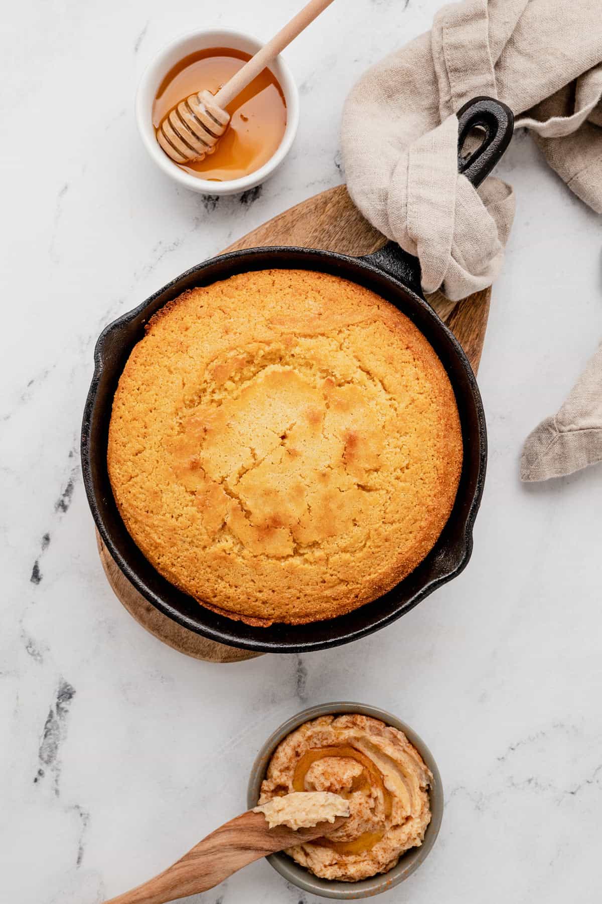 Overhead view of a skillet cornbread with some honey and honey butter on the side.