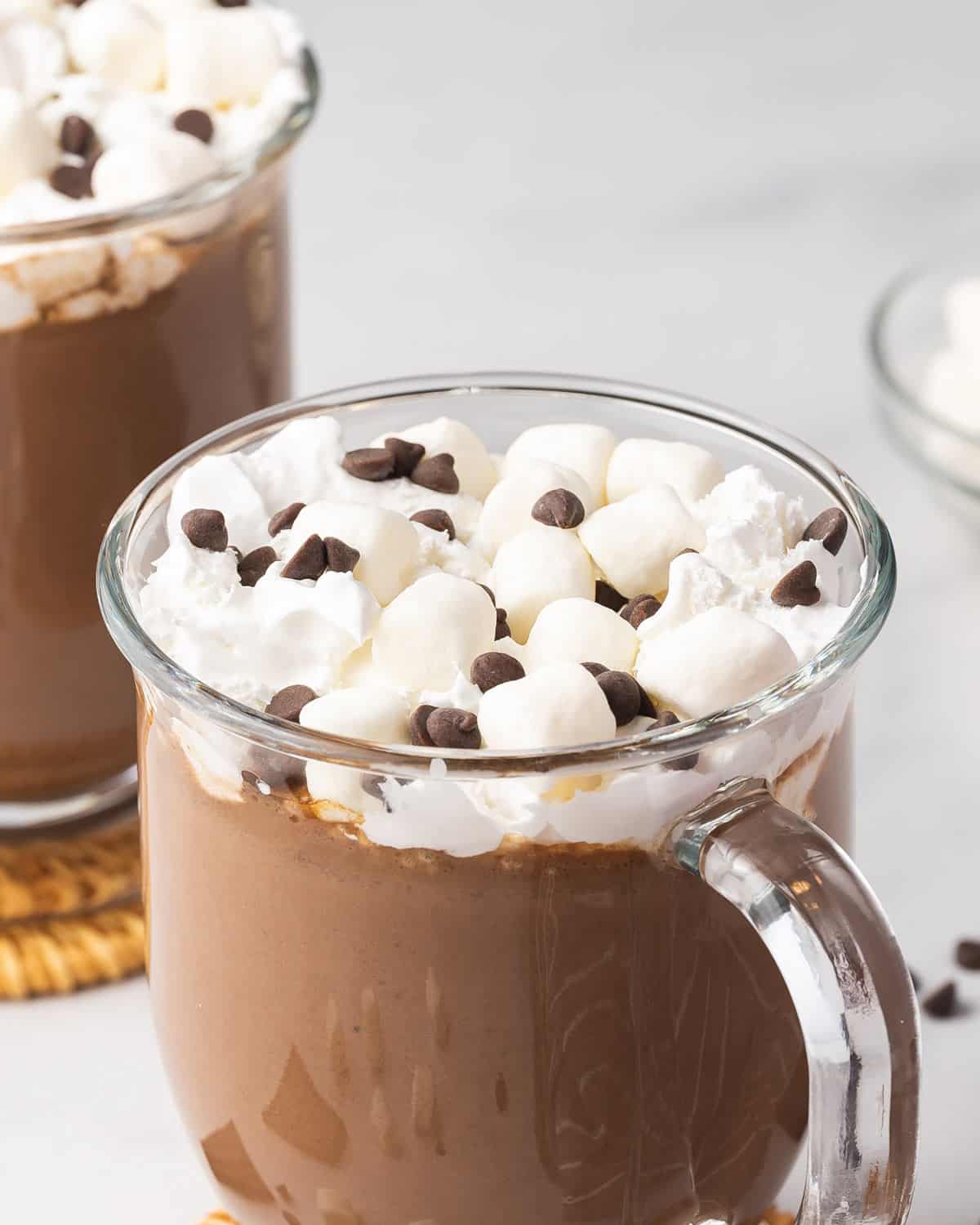 A glass mug of crockpot hot chocolate with whipped cream, mini marshmallows, and chocolate chips.