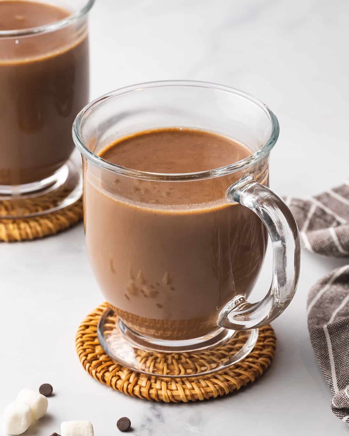 A clear mug of crockpot hot chocolate on a coaster.