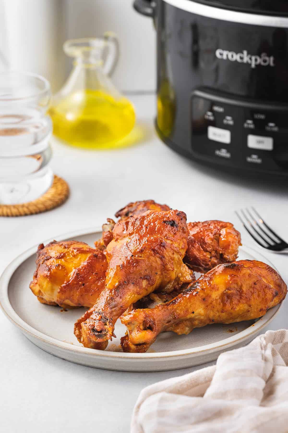 A plate of multiple slow cooker chicken drumsticks with a crockpot in the background.