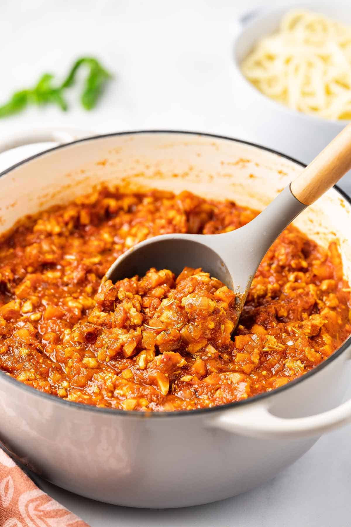 A pot of chicken bolognese with a ladle.