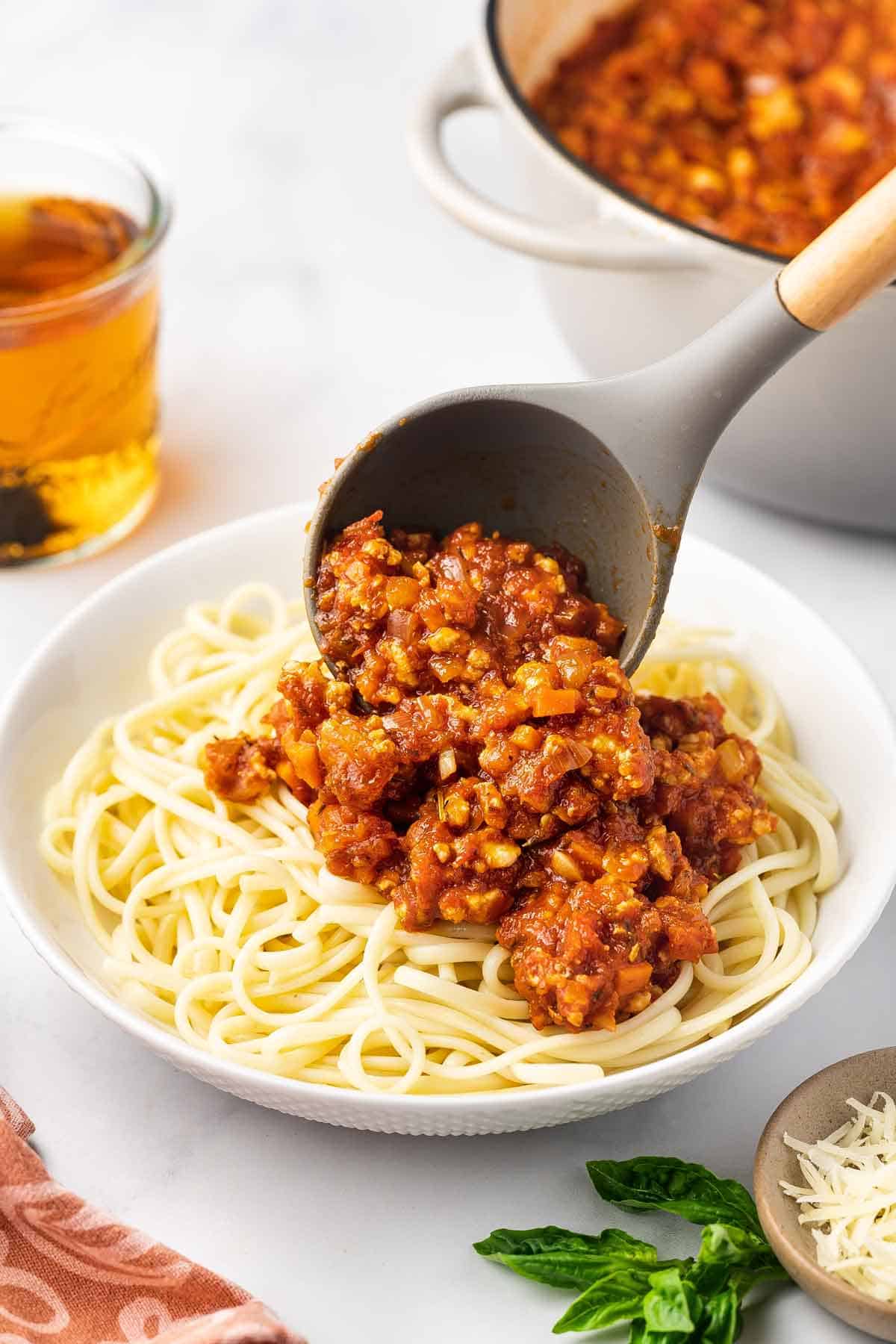 A spoonful of ground chicken bolognese spooned over a plate of noodles.